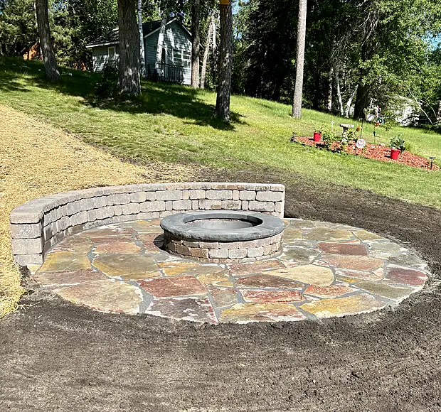 Circular flagstone fire pit patio with a curved block seating wall around the ring