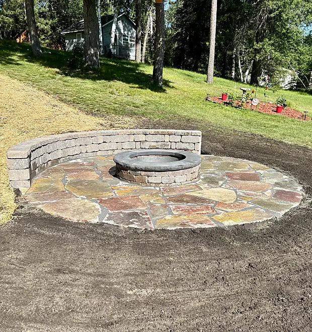 Round flagstone fire pit surround with a block seating ring on a sloped lawn