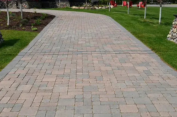 Wide paver walkway with a contrasting border running between mowed lawn and planting beds