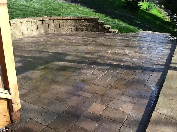 Rectangular paver patio bordered by a tan block retaining wall with built-in steps