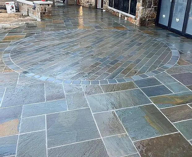 Large bluestone patio with a radial circular inlay set beside a stone-clad lake home