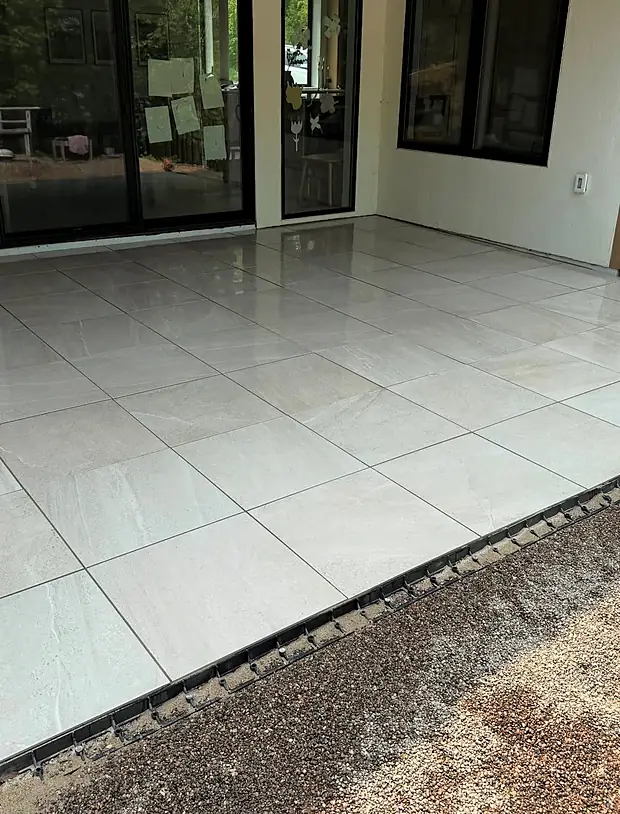 Light grey porcelain paver terrace laid tight against a home with an edge restraint and gravel border