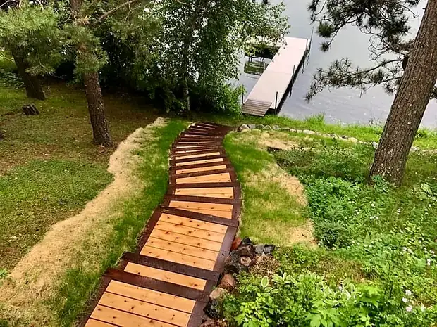 Curving cedar stairway descending a grassy shoreline slope to a dock on the lake