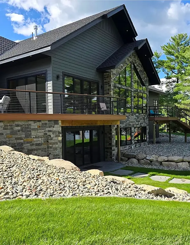 Lake home with a boulder retaining wall, river rock beds and flagstone stepping stones set in new lawn