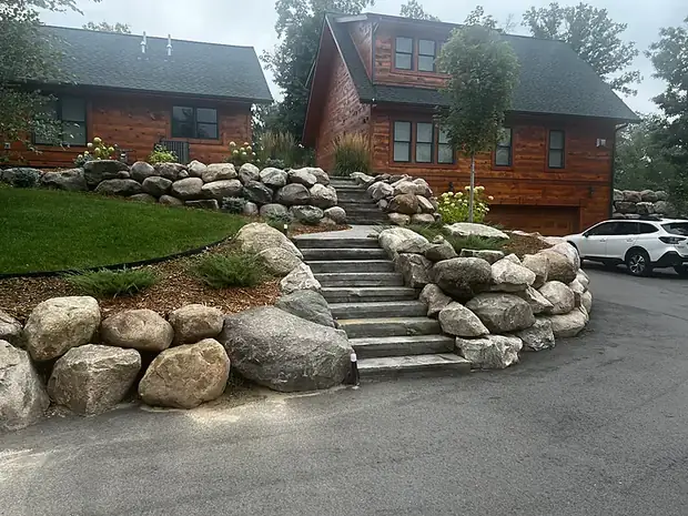Long stone stairway climbing between large boulder retaining walls to a log home entry
