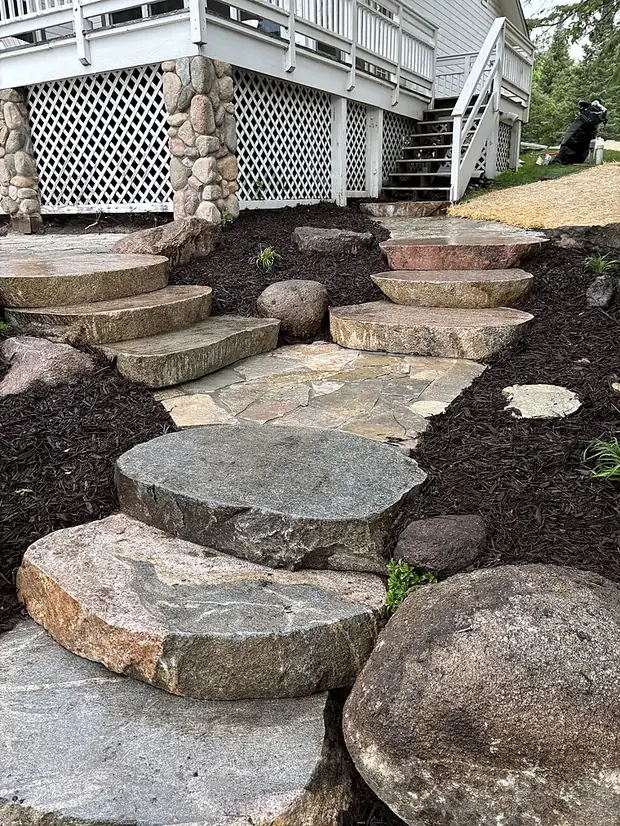 Irregular natural stone slab stepping stones set through dark mulch beds beside a deck