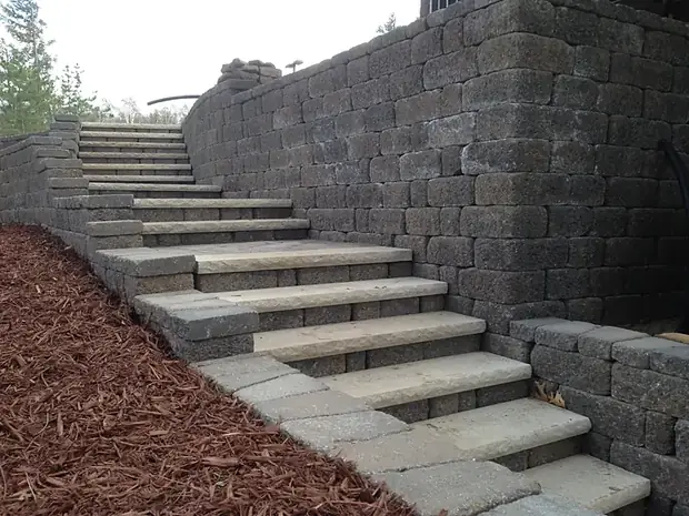 Long run of block steps with cut stone treads rising alongside a charcoal segmental block wall