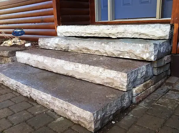Thick quarried limestone slab steps with rough split faces leading to a log cabin door
