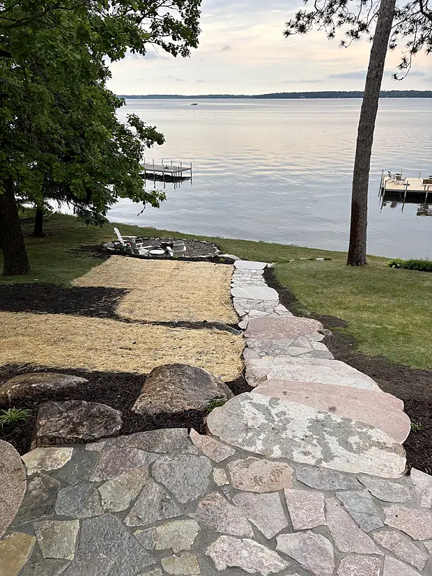 Flagstone stepping path edged with boulders running down a lawn to a dock at sunset