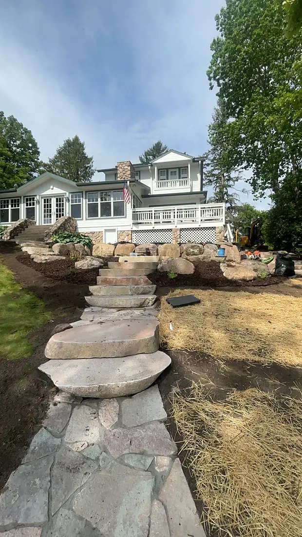 Wide natural stone slab steps and a flagstone landing climbing to a white lake home
