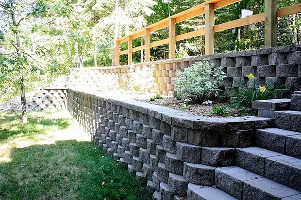 Long curved segmental block retaining wall with stone steps and a terraced planting bed