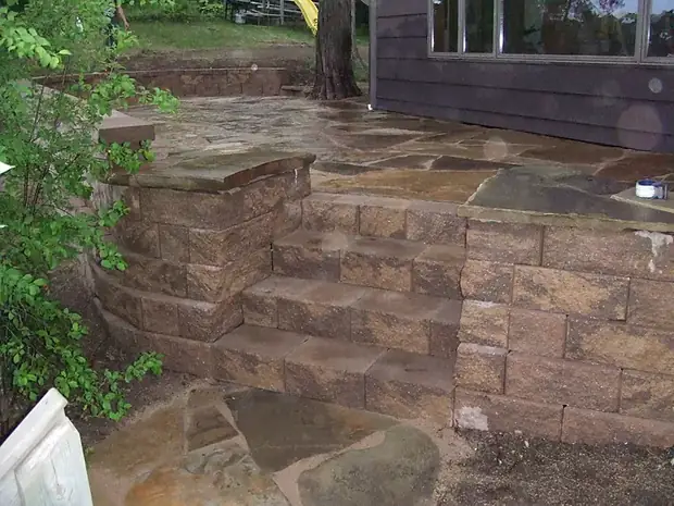 Brown block seating wall with stone steps connecting to a flagstone patio